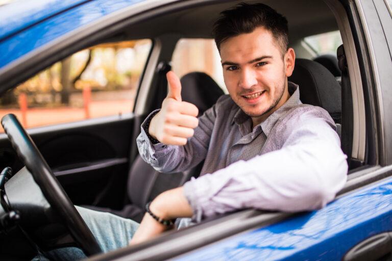 Happy man sitting inside car showing thumbs up. Handsome guy excited about his new vehicle. Positive face expression
